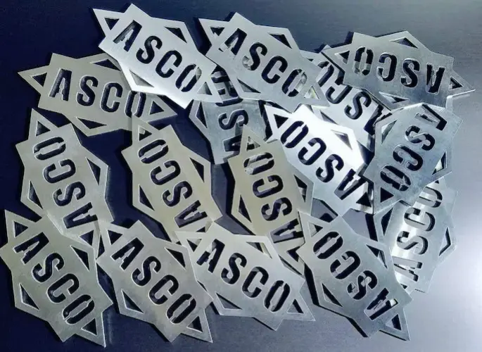 Several metal cutouts of the Aluminum Supply Company (ASCO) logo rest in a pile.