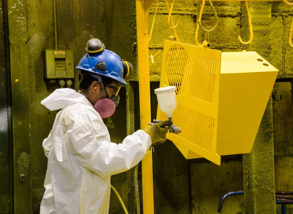 A worker sprays a metal piece yellow.
